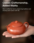 Red ceramic teapot held in a hand with text about craftsmanship and tradition.