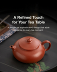 Red ceramic teapot on a dark surface with text about its design.