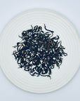 Loose-leaf Heng Yin Hion Almond Aroma DanCong Oolong tea displayed on a white ceramic plate, showcasing twisted high-mountain Phoenix DanCong leaves.