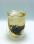 Moonlit Magnolia DanCong Oolong cold brew tea bag steeping in a clear glass with ice, showcasing the floral aroma and amber infusion.