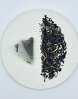 Loose-leaf Silent Jasmine DanCong Oolong displayed beside its pyramid-mesh cold-brew tea bag on a ceramic plate.