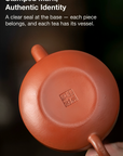 Red ceramic teapot with a clear seal at the base on a dark background