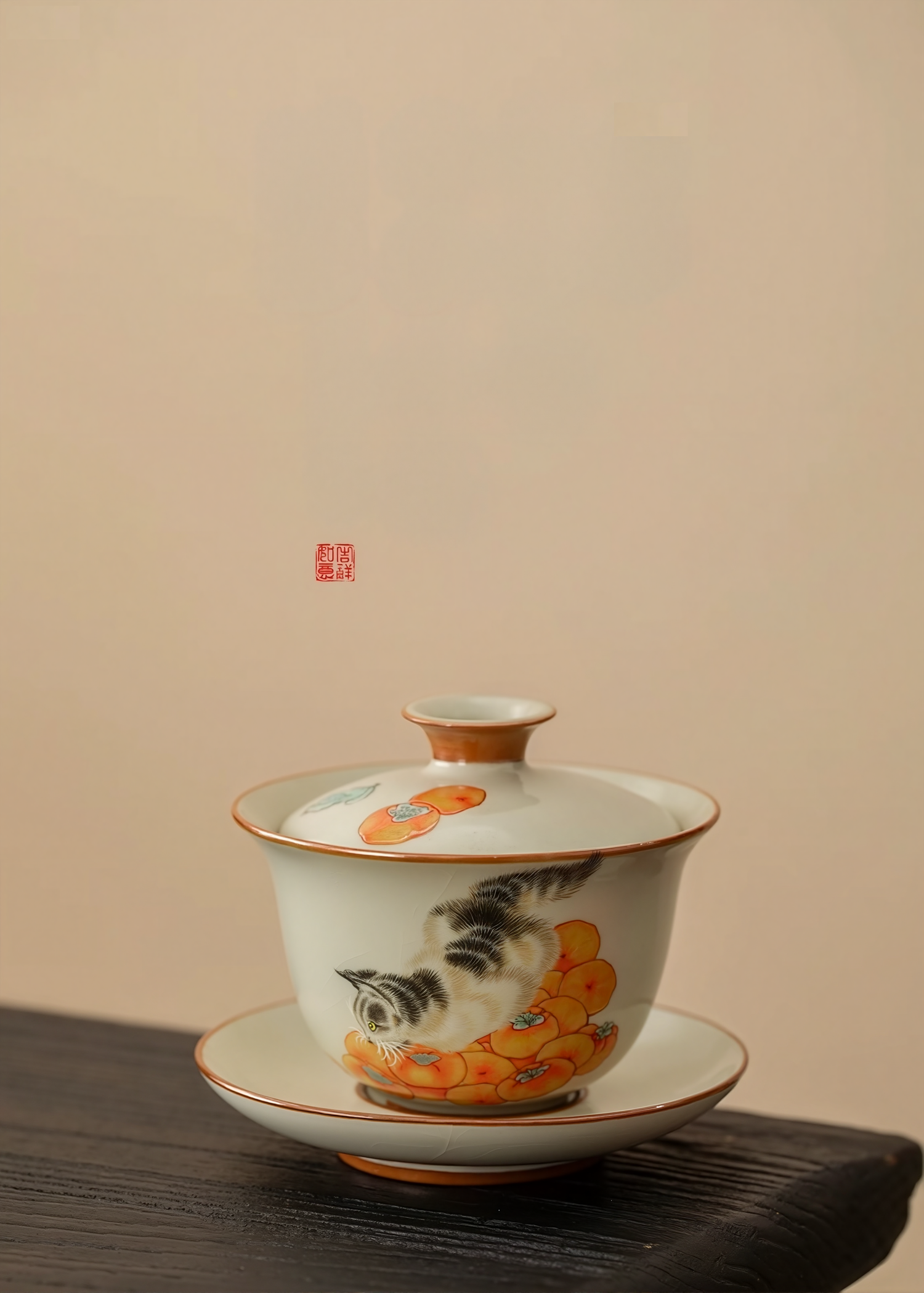 Porcelain gaiwan (lidded bowl) with hand-painted cat and persimmon design, placed on a wooden surface against a beige background