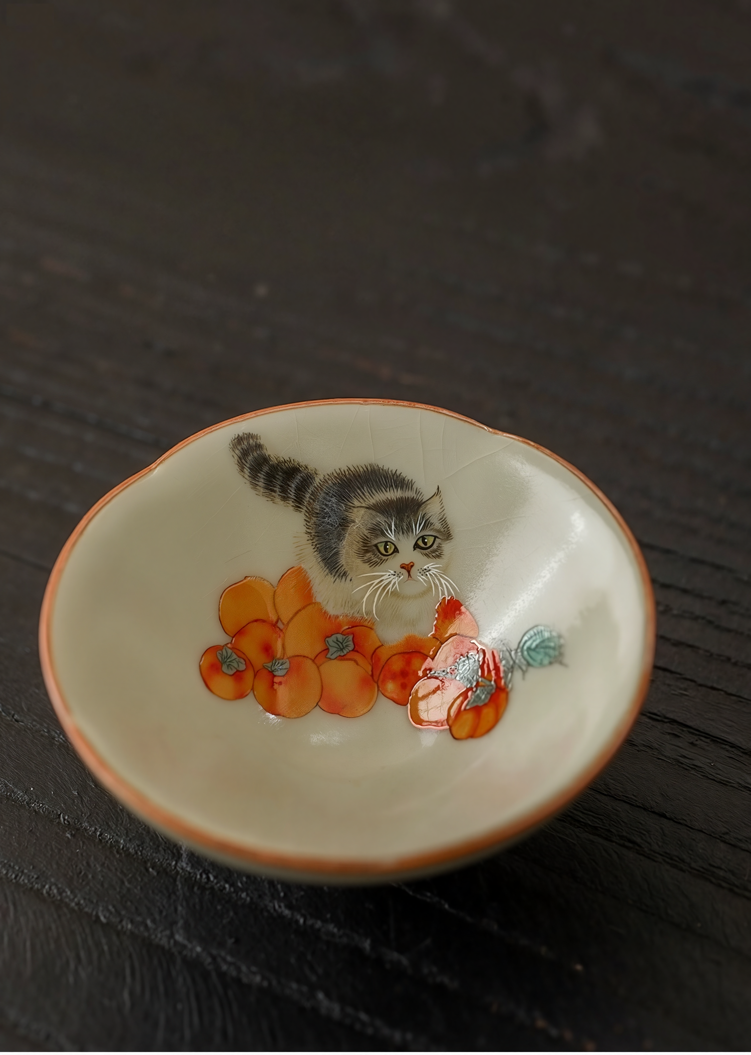 Hand-painted ceramic douli teacup with kitten and persimmon design on a dark wooden surface
