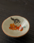 Hand-painted ceramic douli teacup with kitten and persimmon design on a dark wooden surface