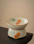 Porcelain tea strainer with hand-painted persimmon design, placed on a wooden surface