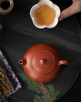 Red teapot with a white cup of tea on a dark surface