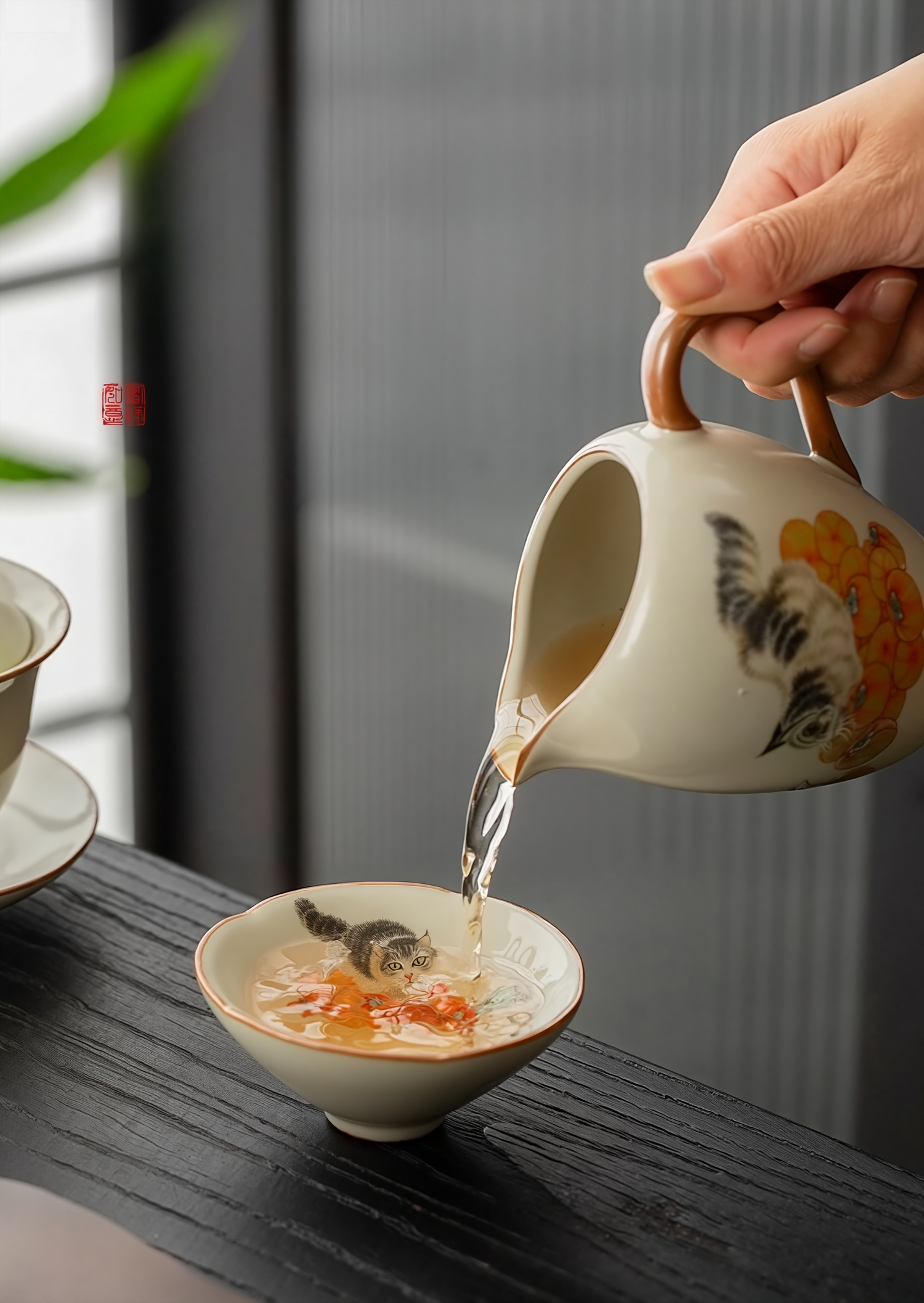 Pouring tea from a hand-painted ceramic fairness pitcher into a douli teacup with kitten and persimmon design on a wooden table