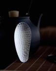 Hammered stainless steel tea scoop (8.3 × 3.5 cm) resting on a teapot lid, photographed against a dark background.