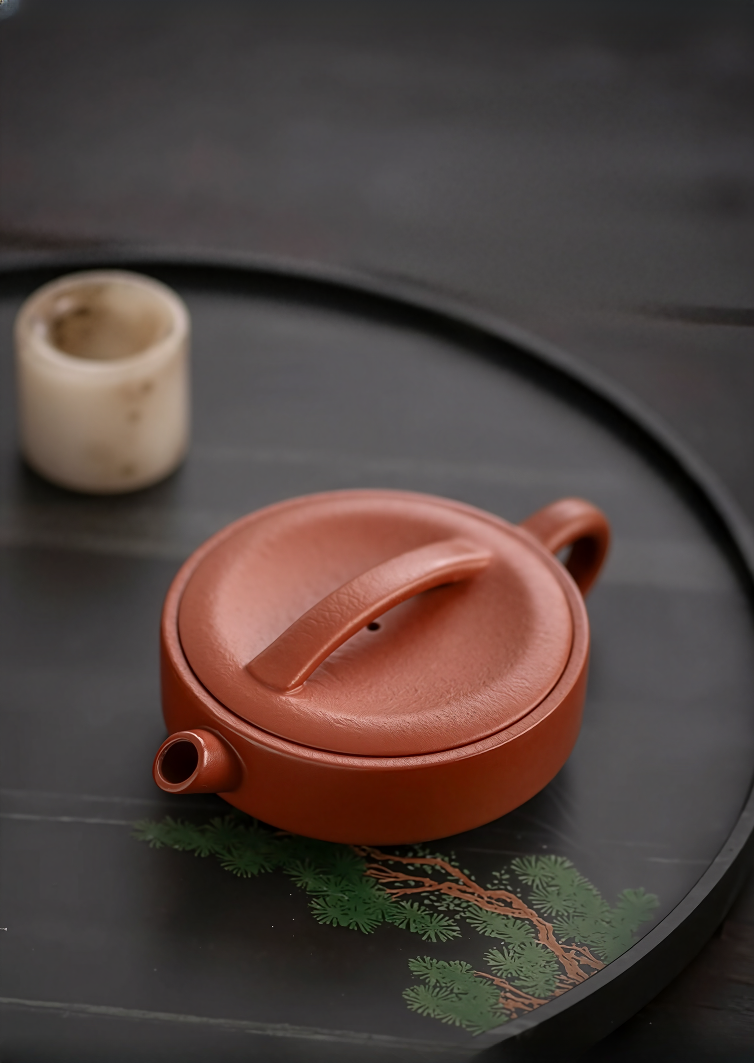Red clay teapot on a dark surface with a small white cup in the background