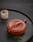 Red clay teapot on a dark surface with a small white cup in the background