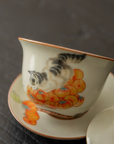 Porcelain gaiwan with hand-painted cat and persimmon design, placed on a dark background