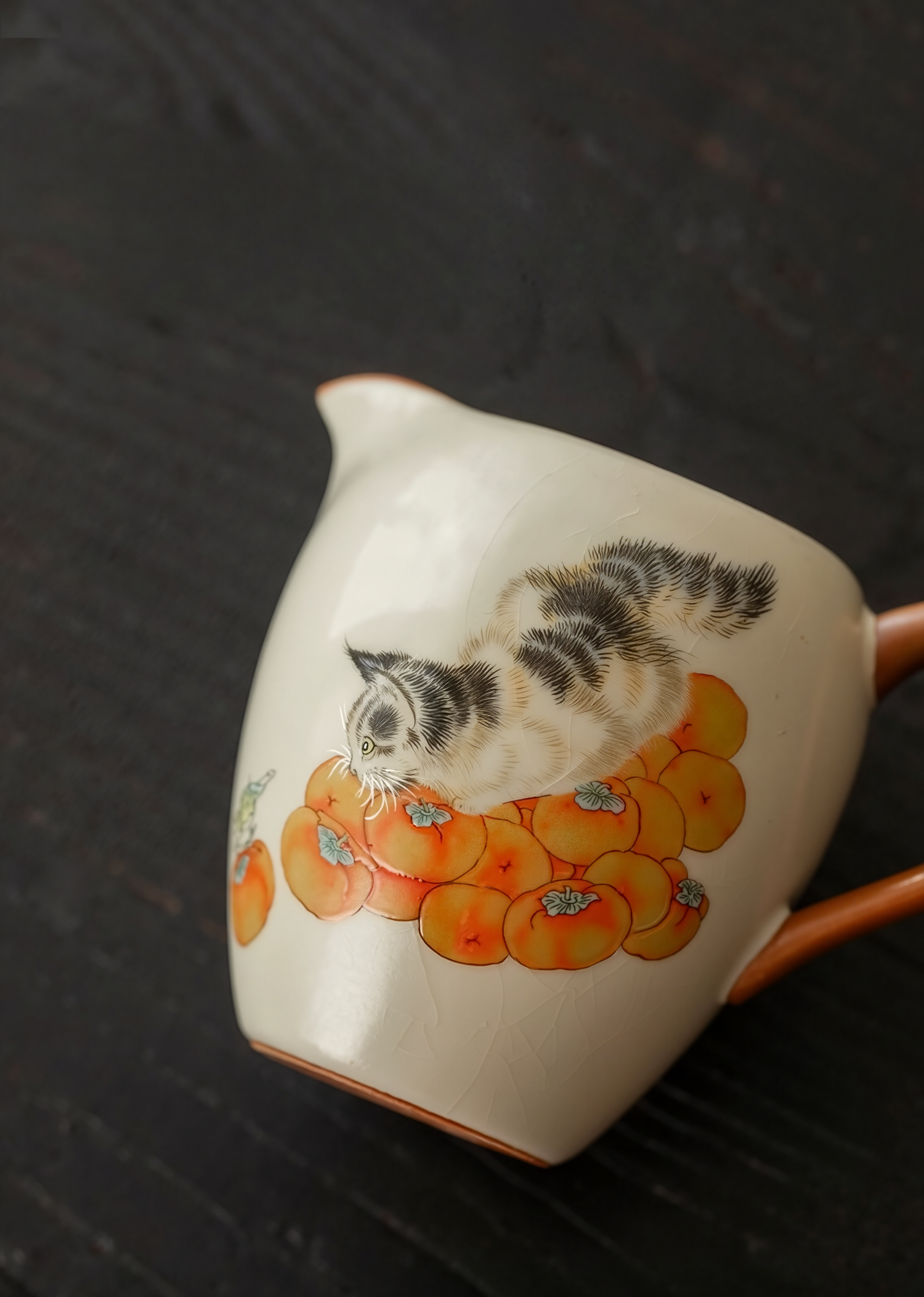 Porcelain fair cup (gongdao bei) with hand-painted cat and persimmon design, placed on a dark surface
