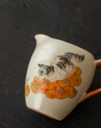 Porcelain fair cup (gongdao bei) with hand-painted cat and persimmon design, placed on a dark surface