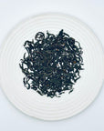 Loose-leaf Geng DanCong Golden DanCong Red-Style Oolong showing twisted Phoenix Mountain DanCong tea leaves on a white plate.