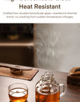 Glass tea set with steaming tea on a wooden table, featuring text about high borosilicate glass.