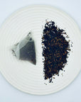 Silken Orchid Dancong Oolong ingredients displayed: whole-leaf Phoenix Mountain oolong next to a pyramid cold brew tea bag on a white plate.