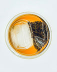 Top view of Sunlit Petal DanCong Oolong tea bag and ice gently steeping in cold water, revealing aromatic floral tea leaves.